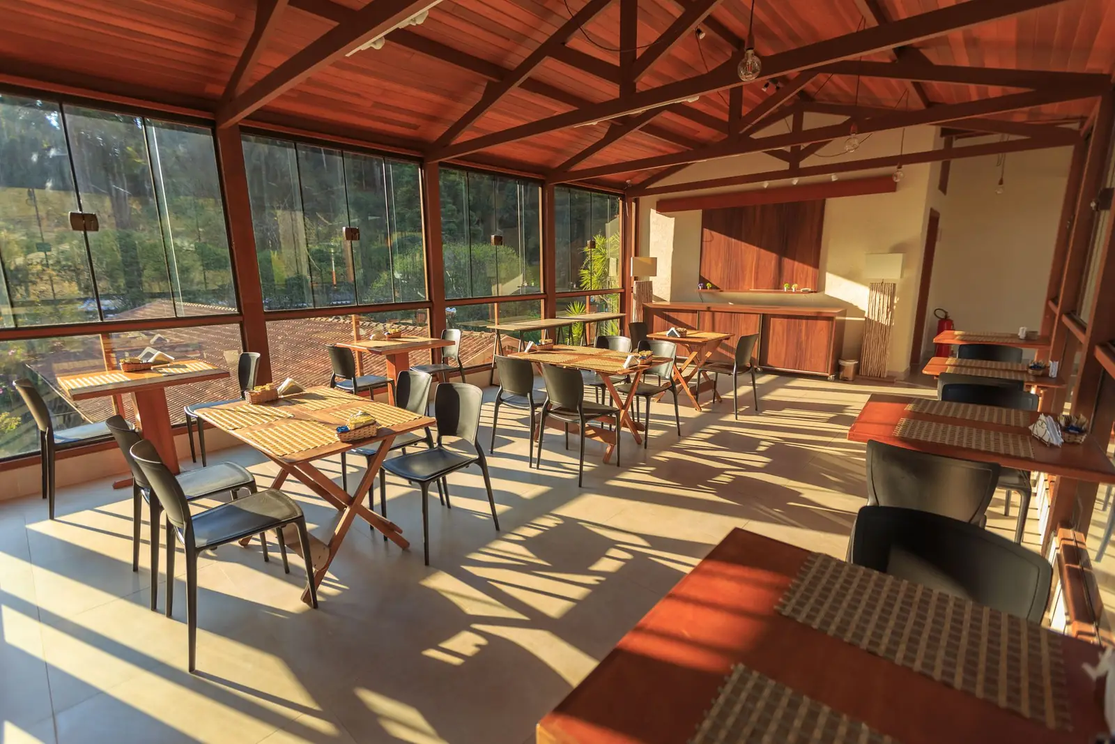 An empty wood-beamed dining room with late-afternoon sun streaming across the tables