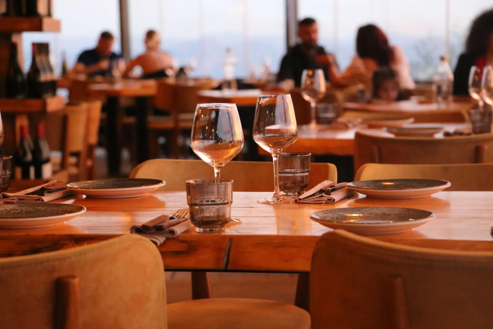 Set wooden tables in a warm restaurant, guests dining by the windows behind